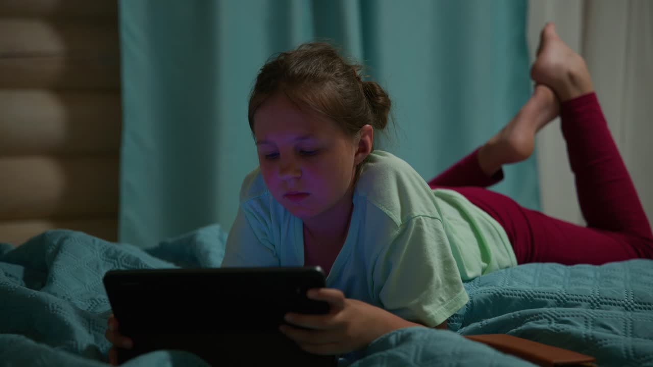 Young Girl Lying on Bed and Using a Digital Tablet