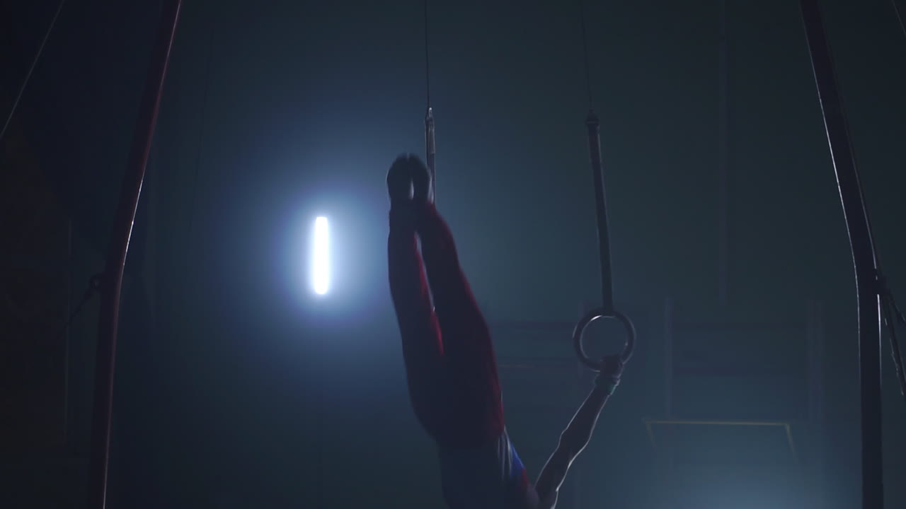 гимнастка на темном фоне стоит на руках, используя кольца в воздухе. выполняет вращение в олимпийской программе в замедленном движении 120 кадров в секунду. гимнастические кольца, профессиональная гимнастка