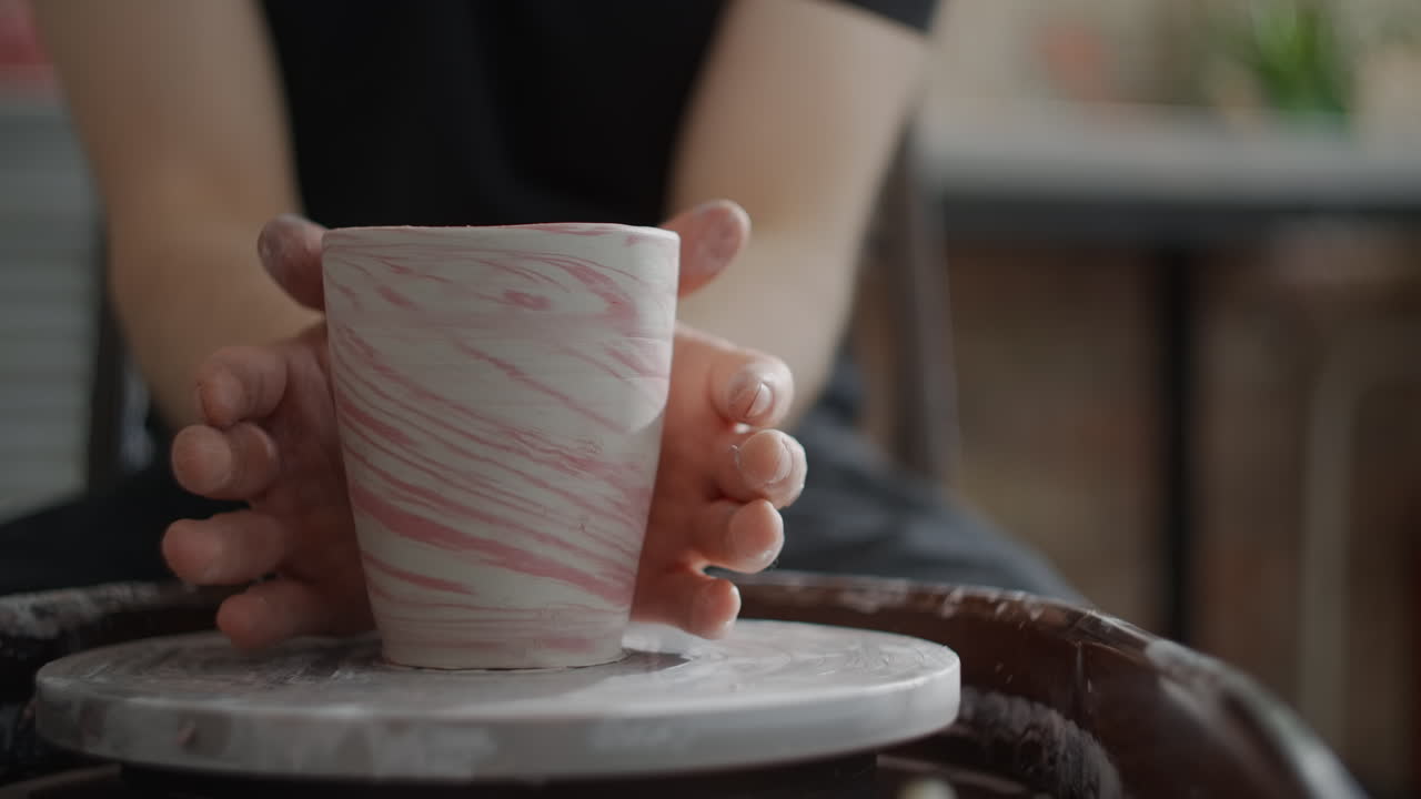 Hands crafting a marbled clay cup on a pottery wheel