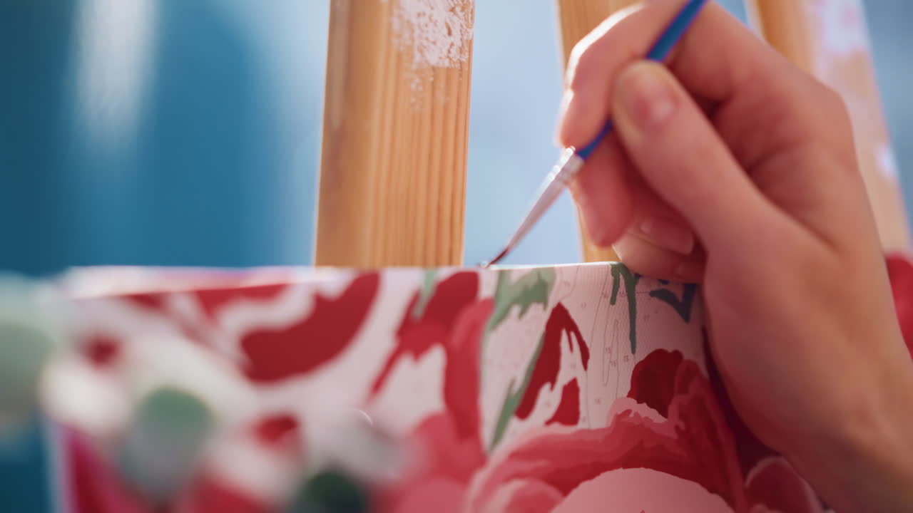 Closeup White Hands Painting Leaf Detail On Floral Canvas, Cool Daylight, Tiny Brush Strokes, Careful Layering Of Greens, Roller Tool In Background, Patient Technique, Intimate Craft Moment