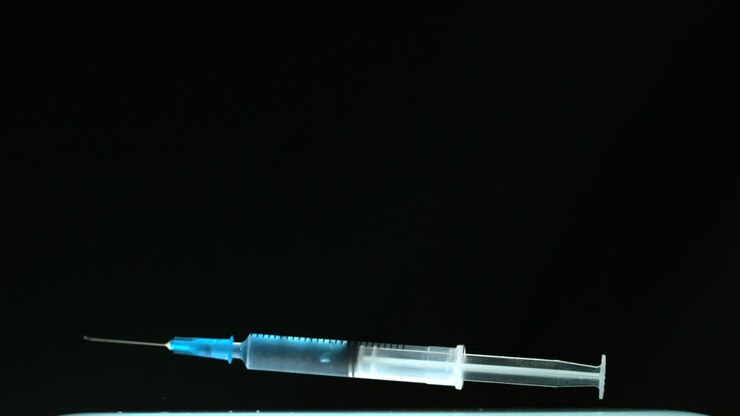 Syringe of blue liquid falling and bouncing on black surface