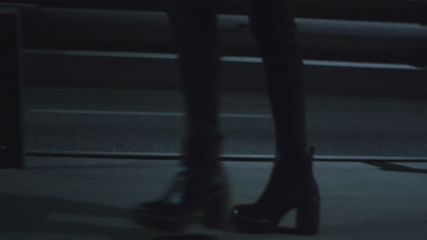 Woman-legs-walking-highway-at-late-night-dark-road-with-passing-cars.