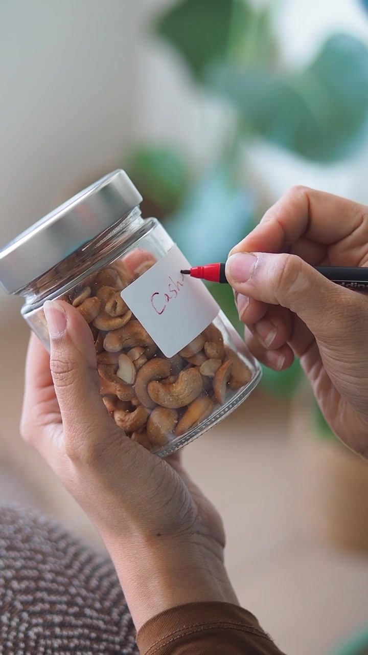Orang Menulis Label Kacang Mete di Stoples Kaca
