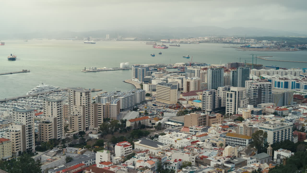 Vista elevata sullo skyline della città e sulla marina di Gibilterra con navi da carico ancorate nella Baia di Gibilterra sotto cieli nuvolosi e drammatici.