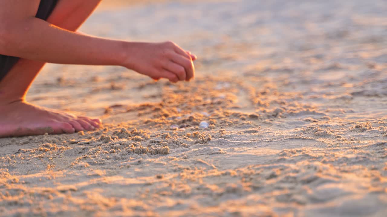Close-up boys hands playing in sand at sunset. Boy putting different pebbles into sand in the evening. Child is having fun during summer holidays.
