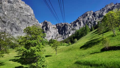 A cable car climbs the mountain in Leukerbad. The landscape is in bloom and everything is green. The Swiss Alps in sunshine and blue skies