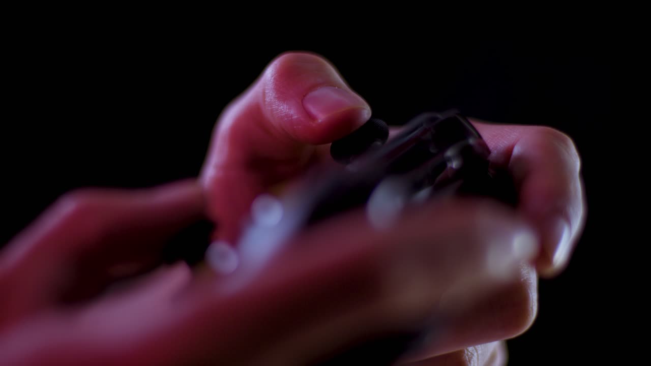 Playing video games in a darkened room with a black background close up on a controller joystick playing slowly soft focus