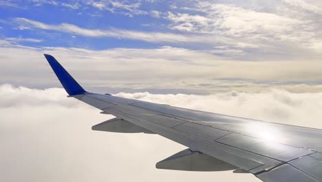 wing of an airplane in flight soaring above and through the clouds in the sunny sky