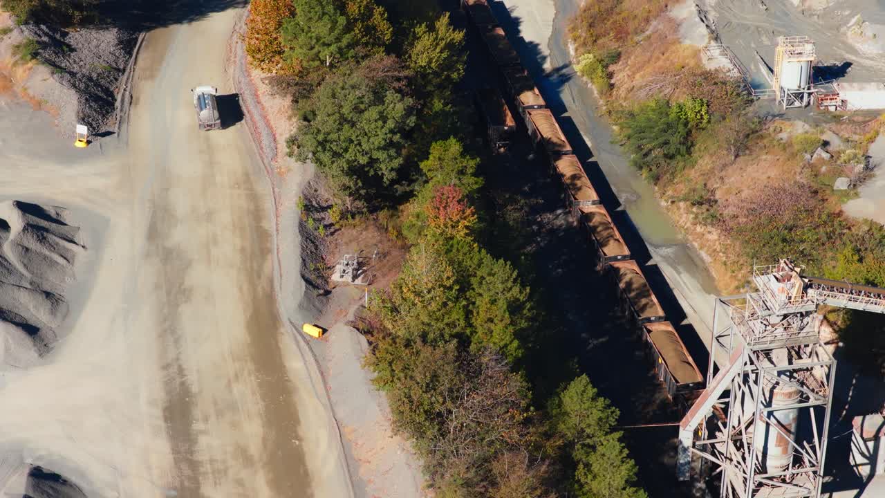 Aerial orbit reveals rail cars and conveyor tower on other side of trees as truck drives away