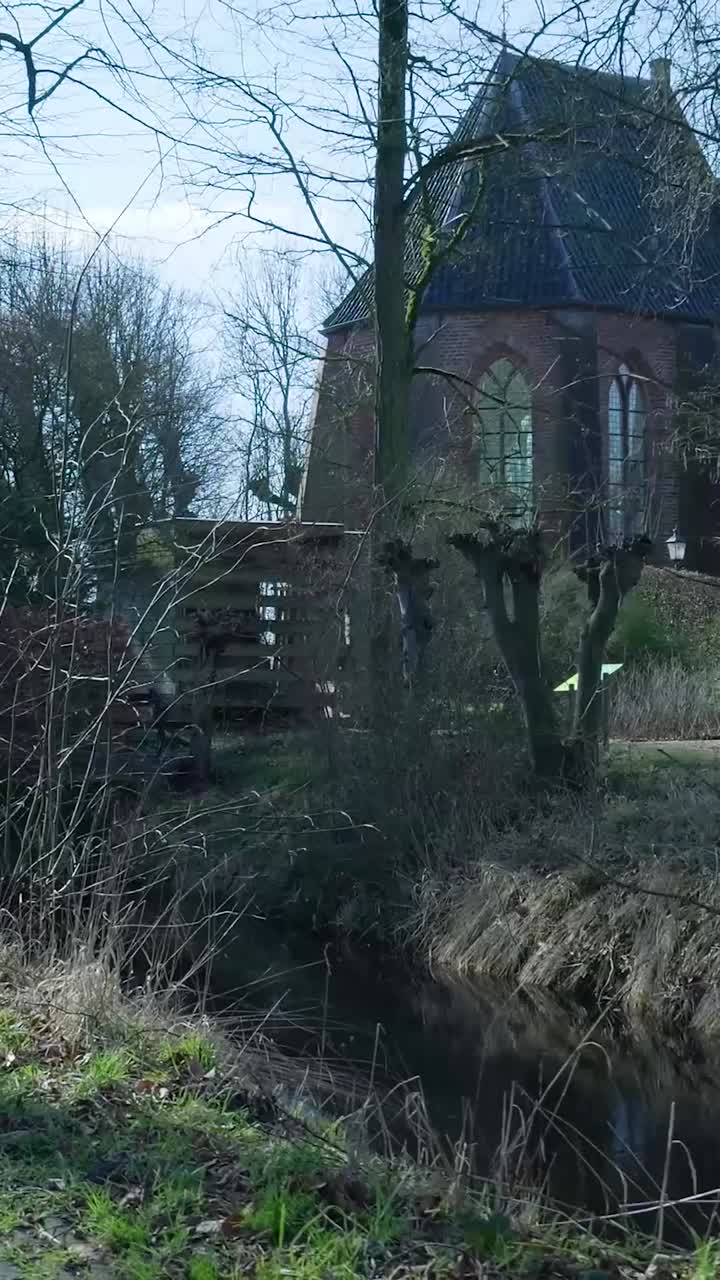 Vecchia chiesa in mattoni riflessa in un ruscello calmo con alberi spogli