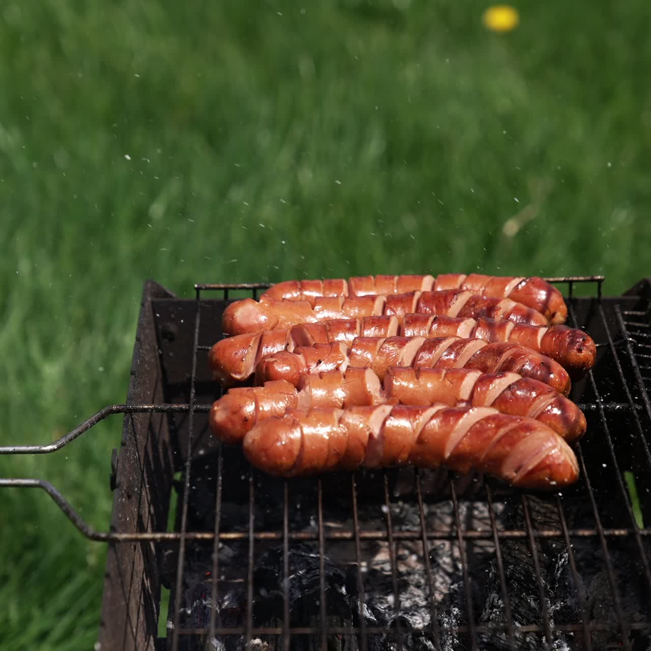 Ready sausages on a grill grate. Cooking barbecue in summer. Grilled sausages for lunch outdoors. Delicious food for picnic