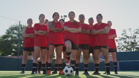 portrait of determined female soccer team with ball on training ground against flaring sun