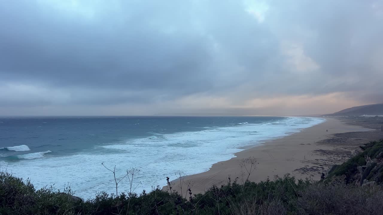 저녁 햇살 아래, 편안하게 휴식을 취하는 사람들이 잔잔한 파도를 즐기는 넓은 해변 풍경