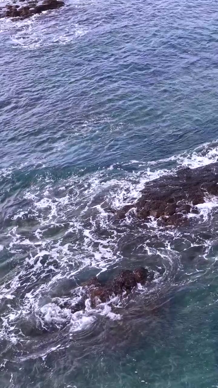 Vista dall'alto di acqua di mare turchese e schiuma bianca che si infrange su scogli costieri scuri
