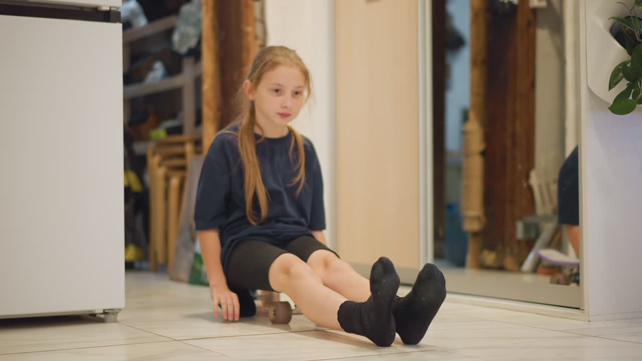 Flicka sitter på köksgolvet, kaukasiskt barn med flätor och svarta strumpor lutar sig mot kylskåpet, fundersam min, varmt inomhusljus, mysig hemmiljö som antyder en tyst paus innan hon hjälper till