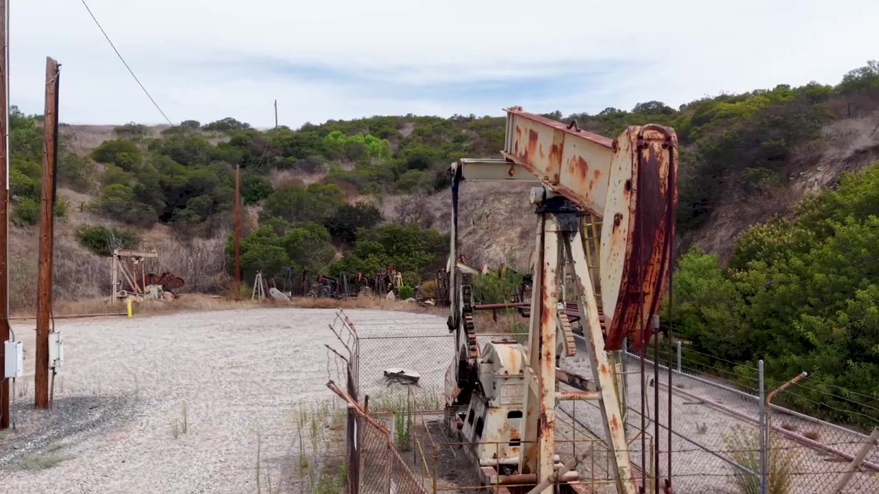 Cerchio aereo ravvicinato a bassa quota attorno a un vecchio cavalletto di pompaggio petrolifero arrugginito nella Contea di Orange, California