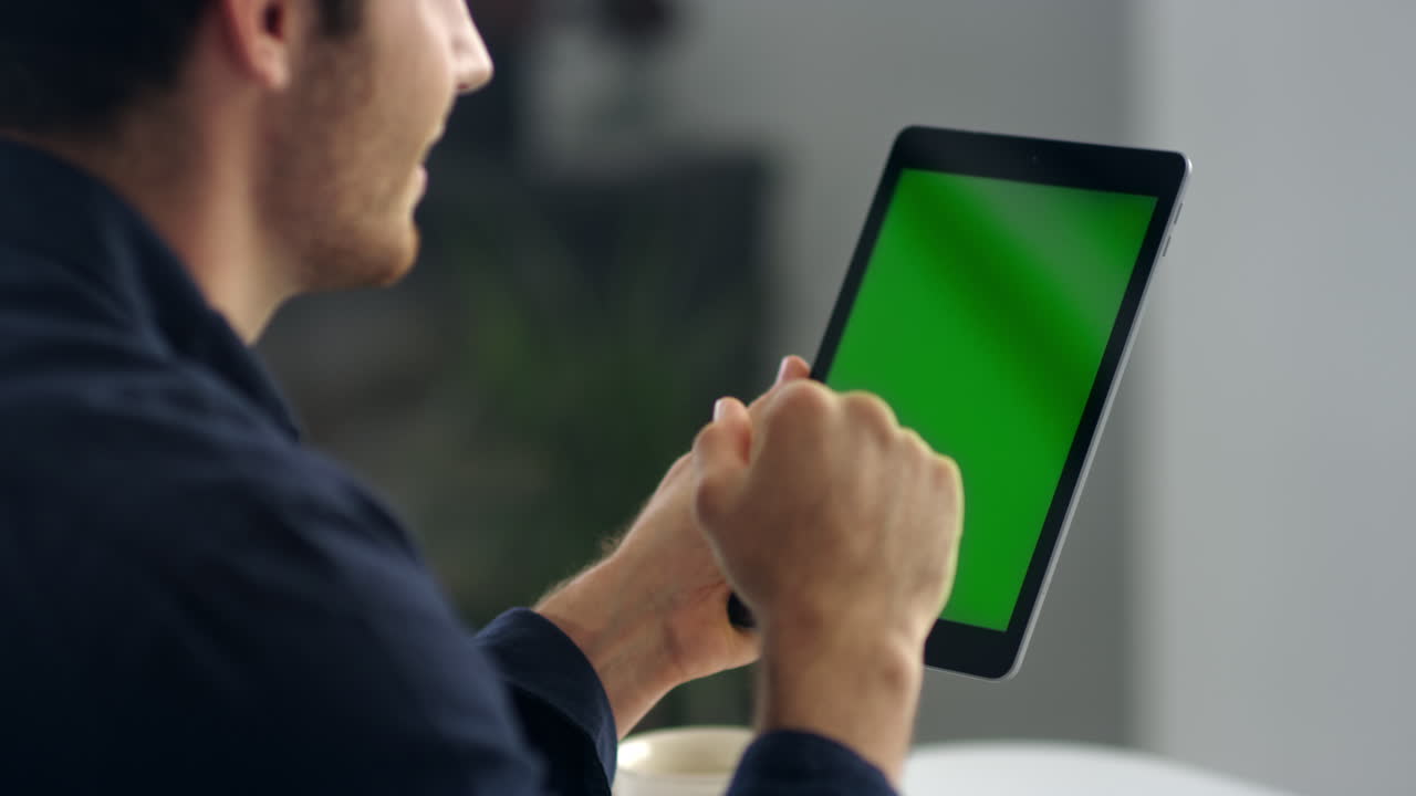 un alegre profesional masculino saludando mientras hace una videollamada con el panel de pantalla verde del celular.