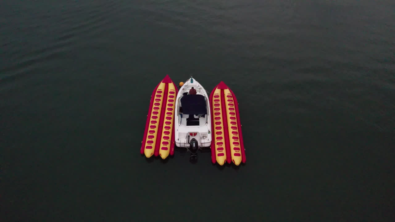 Banana boat next to speedboat, unrecognizable man keeping equipment. Aerial during sunset