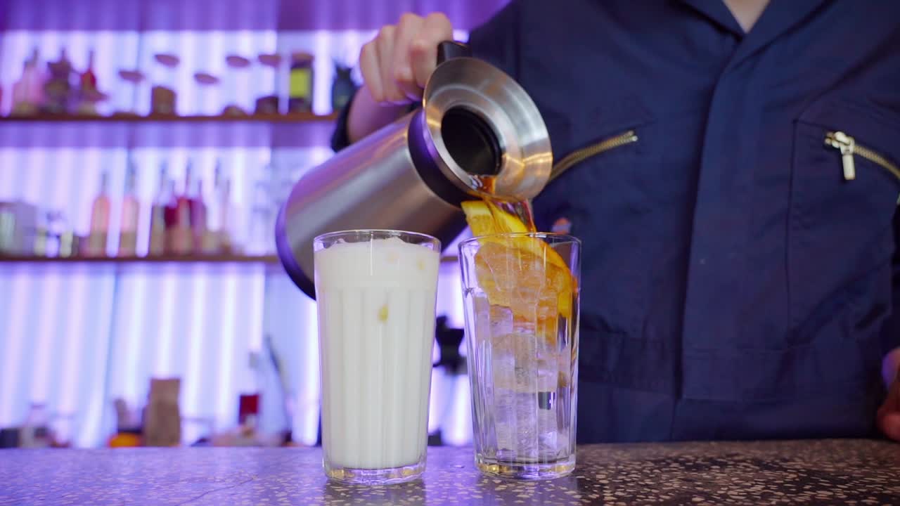Person pouring cold drinks into glasses with ice and orange slices