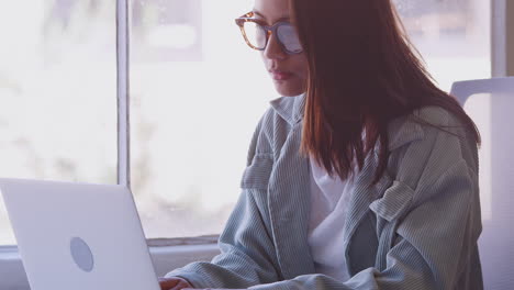 Millennial-Asian-woman-sitting-at-a-desk-in-an-office-using-laptop-computer,-tilt-shot