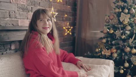 bella dama sonríe en el sofá cerca del árbol de navidad dorado