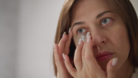 woman strokes skin nourishing patch with finger in bathroom. serious lady uses nourishing cosmetic product under eyes standing at mirror closeup