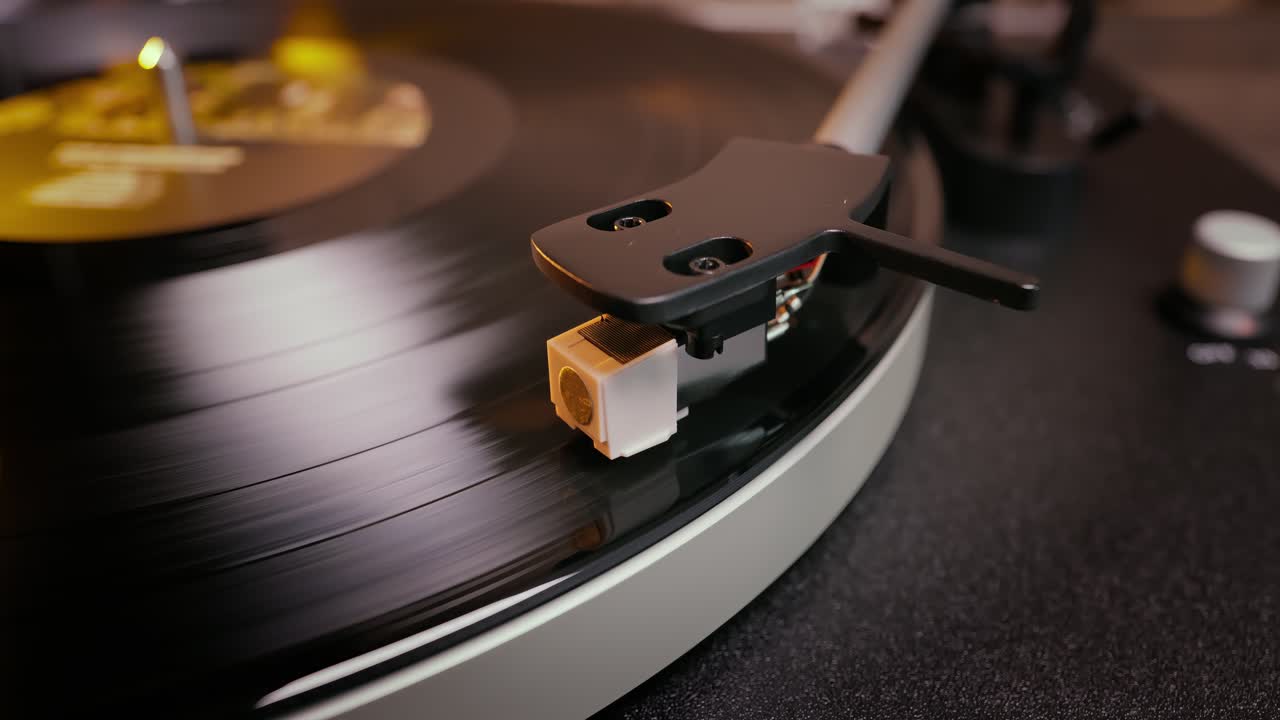 Primo piano dettagliato del braccio di un giradischi con testina bianca, posizionato su un disco in vinile nero sul piatto, che evidenzia la precisione delle apparecchiature audio