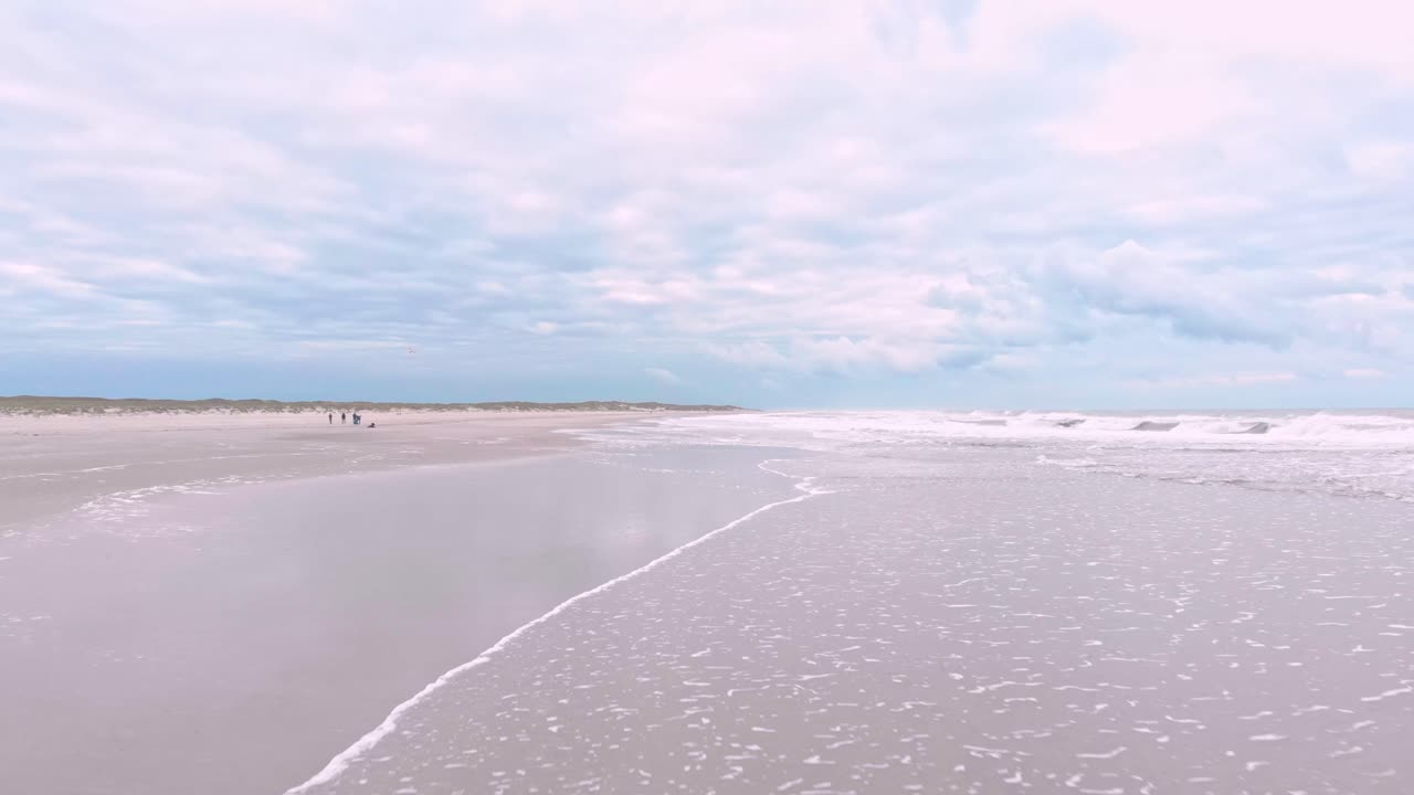 Dronebillede af bølger, der ruller ind over en sandstrand, og indfanger havets naturlige rytme