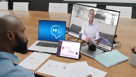 African-american-businessman-in-office-using-computer-with-video-call-and-data-processing-on-screen