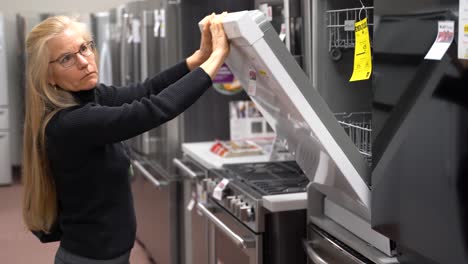 closeup of pretty mature blonde woman looking at dishwashers in a kitchen appliance store