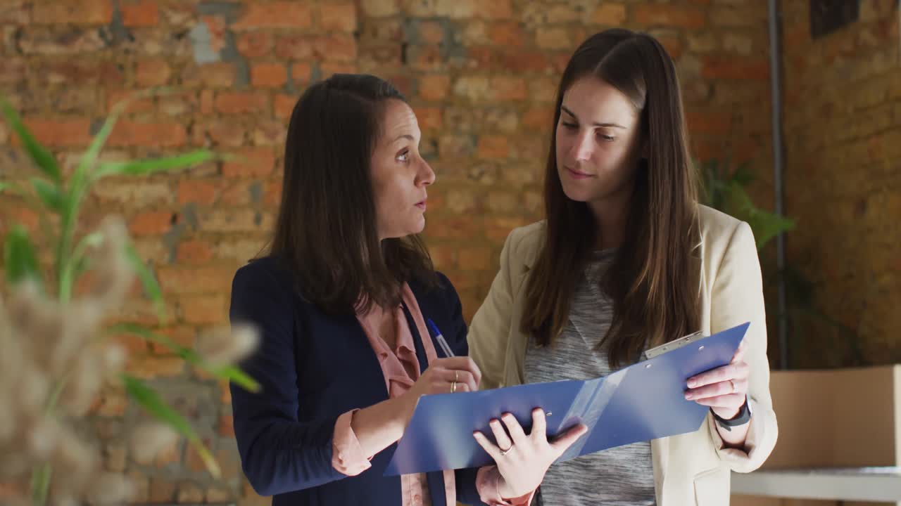 propietaria de un negocio caucásica y su compañera de trabajo hablando de negocios y tomando notas