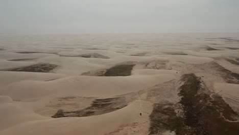 Aerial:-A-truck-with-kitesurfers-traveling-through-the-dunes-of-Lencois-Maranhenses-in-Brazil,-during-dry-season