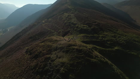 Hiker-on-hillside-with-panoramic-reveal-of-misty-mountains-in-English-Lake-District-UK