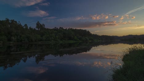 Timelapse-Escénico-De-Día-A-Noche-En-Una-Orilla-Del-Río,-Vista-De-Lapso-De-Tiempo-En-Un-Río-Con-Un-Bosque-En-El-Fondo