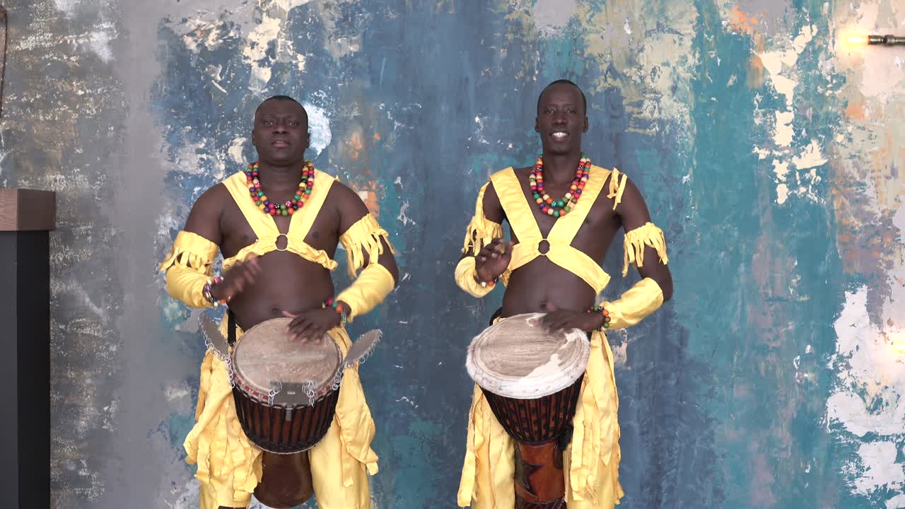 Two African artists in colorful costumes playing djemba drums