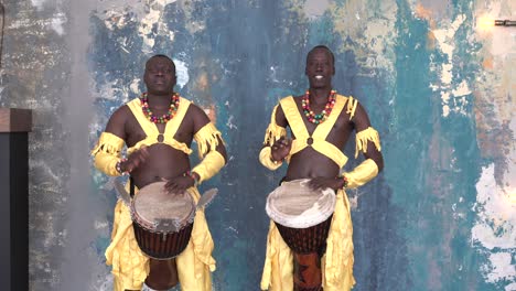 two african artists in colorful costumes playing djemba drums