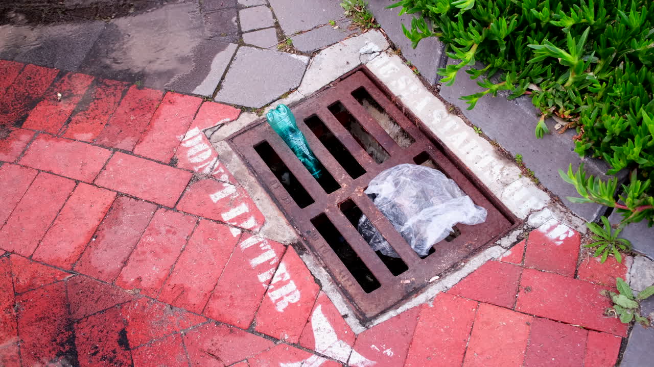 Ironic view of plastic refuse stuck in storm water drainage grate on coastline with stencils warning people to not litter because the ocean starts there