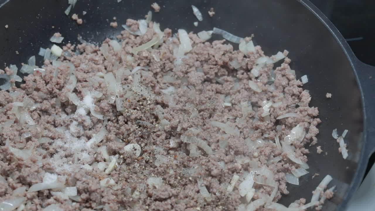 Close-up of salt and oregano being added to minced meat while cooking in a pan