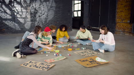 jóvenes activistas ambientales pintando carteles sentados en el suelo