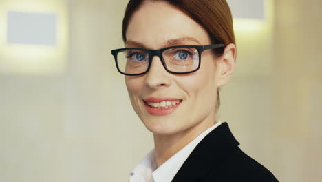 close-up view caucasian businesswoman in formal clothes and eyeglasses looking at the camera and smiling in a meeting room