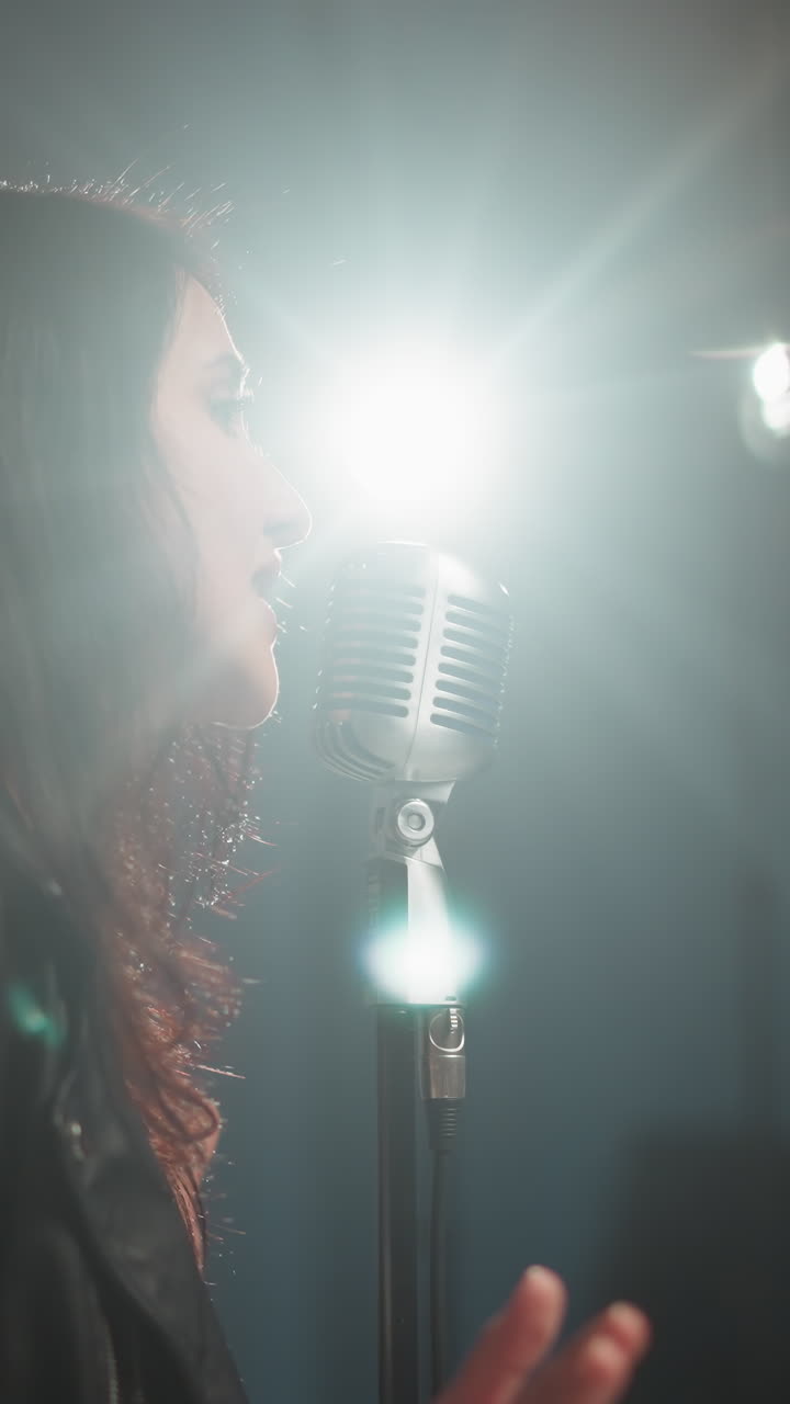 vista borrosa de un cantante y un guitarrista, ambos vestidos de negro, sentados y actuando en una habitación débilmente iluminada. el cantante está posicionado cerca de un micrófono vintage, con iluminación suave