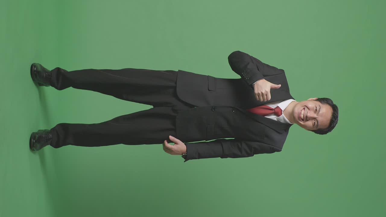 그린 스크린 스튜디오에 서 있는 동안 엄지손가락을 올려 놓고 미소 짓는 아시아 사업가의 몸이 가득 차 있습니다.