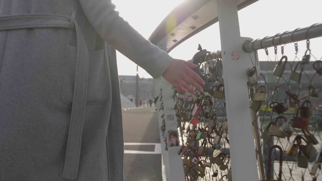 젊은 여성 관광객은 아침 햇살에 다리에 있는 사랑의 자물쇠를 만진다