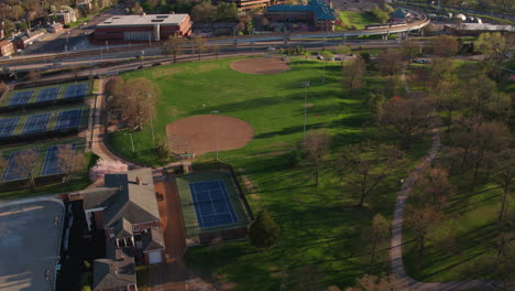 drone flies over city park with baseball diamonds and tennis courts