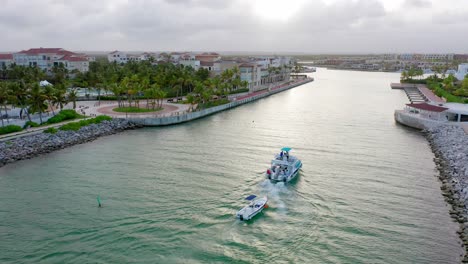 Aerial-view-catamaran-entering-the-marina-of-cap-cana-at-dusk,-towing-small-boat