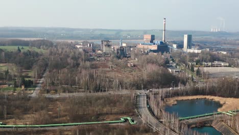 an industrial coal mine complex surrounded by greenery, with tall chimneys belching smoke, large buildings and a road running through the countryside