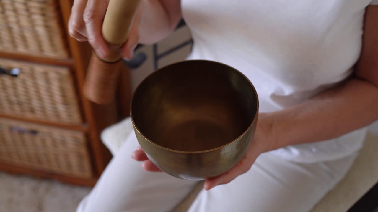 Person Uses Wooden Mallet To Play Brass Tibetan Singing Bowl. Calming Vibrations For Mindfulness. closeup shot