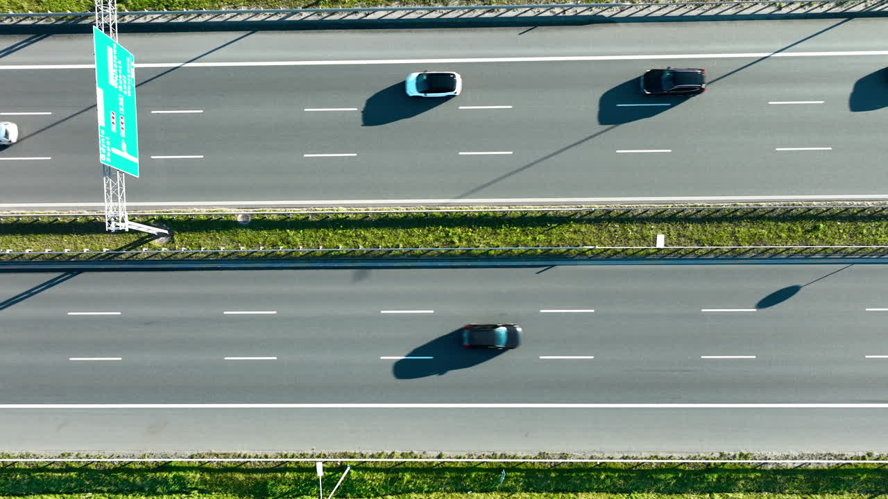Aerial view of multi‑lane highway with directional road sign and moving cars in bright daylight