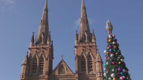 pan up cathederal in sydney with a well decorated christmas tree infront.