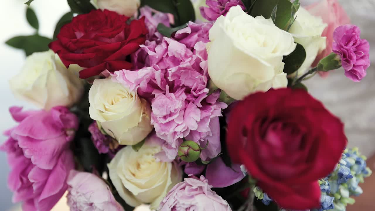 Primo piano di una sposa nel suo abito da sposa che tiene un bouquet di fiori bianchi, rossi e rosa nelle mani, all'aperto, 1080p 60fps